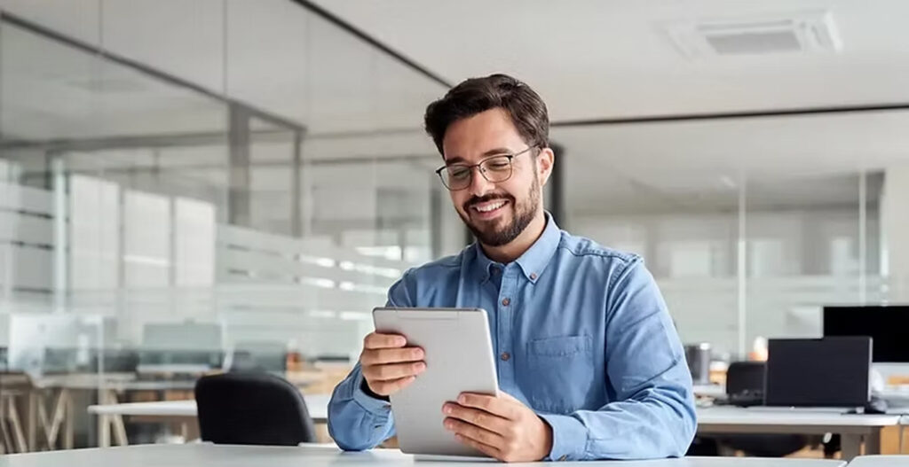 Smiling businessman using a digital tablet in a modern office for remote work and online collaboration.