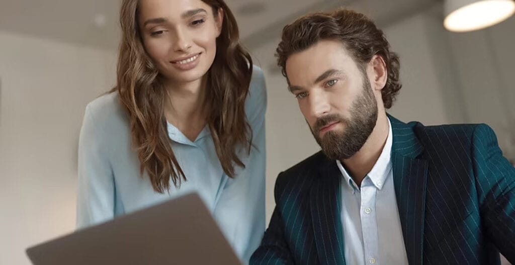 Two professionals collaborating on a laptop, discussing remote work and teamwork solutions in a modern office setting